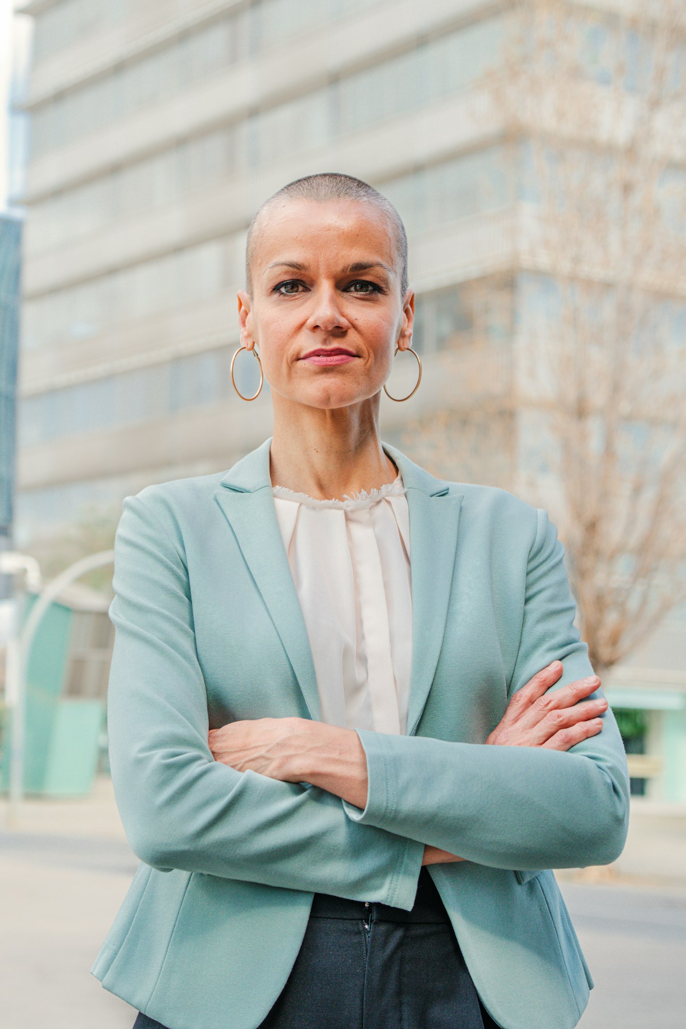 Vertical portrait of successful business woman standing arms crossed at workplace looking at camera