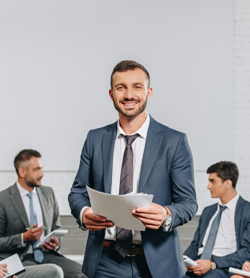 happy business coach standing in front of businesspeople at training in hub